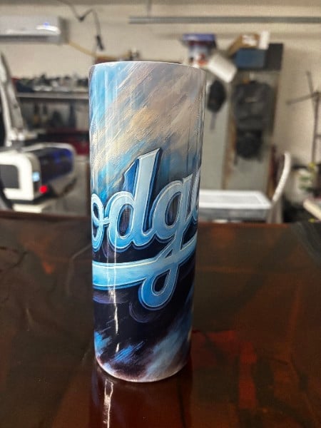 A tall cylindrical drink can with blue Dodgers branding on a desk in a home office setting