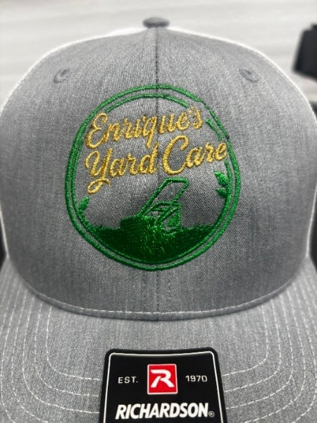 Gray baseball cap with green circular emblem featuring yellow Enriques Yard Care text and leaf design, Richardson brand label visible