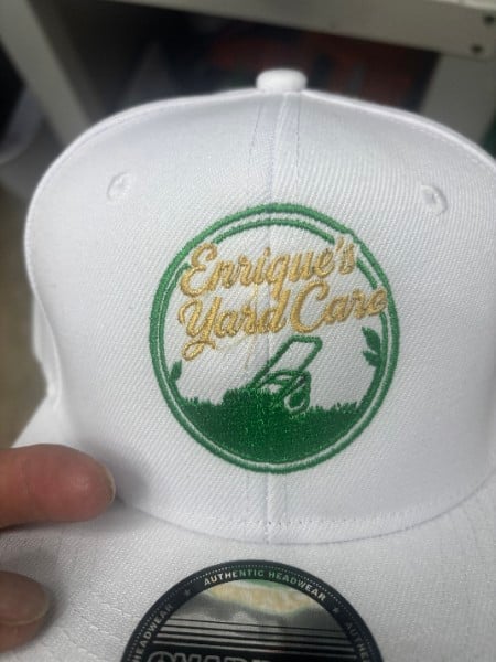 White baseball cap with green circular emblem featuring gold script text reading Pineapple Golf Club, held in someones hand