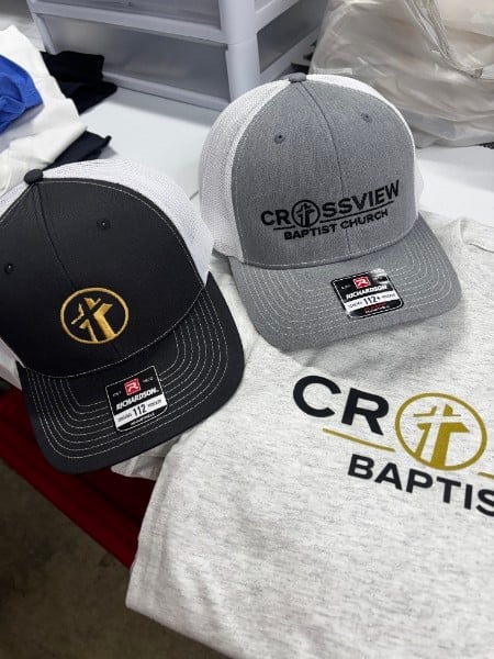 Two Crossview Baptist Church branded caps displayed on a white surface