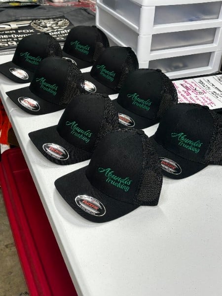 Multiple black mesh trucker caps with green embroidered text displayed on a white table with red trim