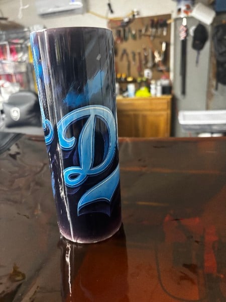 Tall black and blue decorative cylinder with ornate swirling design on a workbench in a garage workshop setting