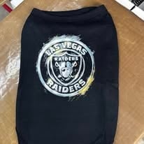 Black dog sweater with Las Vegas Raiders circular logo and text on wooden floor